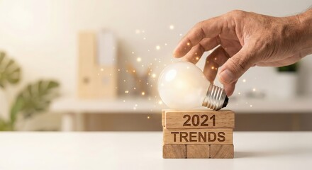 Caucasian adult man hand holding a glowing lightbulb over wooden blocks spelling 2021 trends indoors, innovative business concept for future growth and creative strategy, positive mood.