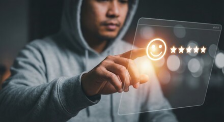 Southeast Asian adult man in a grey hoodie providing five-star customer feedback on a glowing digital interface with a happy emoji icon, indoor setting, positive user experience concept.