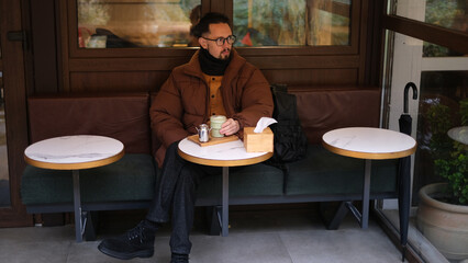 Young man in a jacket sits on an open cafe terrace on an autumn day drinking matcha latte