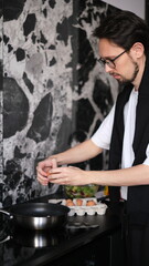 Young slim brunette man cooking scrambled eggs for breakfast in his modern stylish kitchen early in the morning