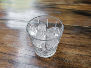 minimal scene of glass with ice on wooden floor