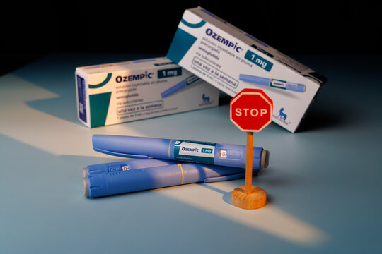 Close up of Ozempic 1 mg semaglutide pens with a wooden stop sign and boxes on a blue background for diabetes and health risk themes.  In Barcelona - Spain, January 10, 2026.