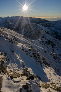 View of a sunburst piercing through snow-dusted peaks, casting long shadows across the alpine landscape, Tri Kopy, Zilina Region, Slovakia.