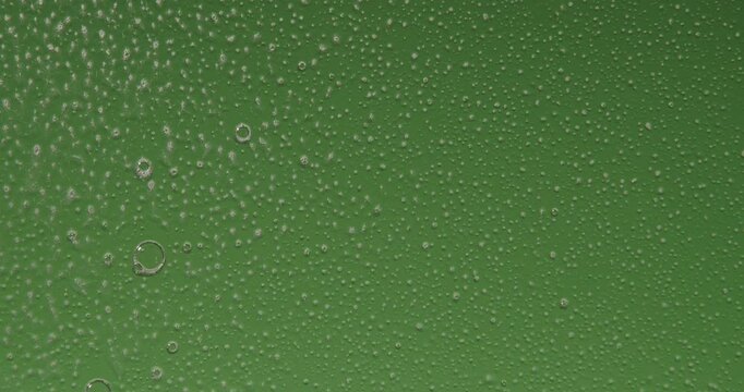 Hand spraying cleaning fluid from a spray bottle onto glass and wiping condensation from a green glass surface. Water droplets and moisture remain on the fogged window. Slow motion.