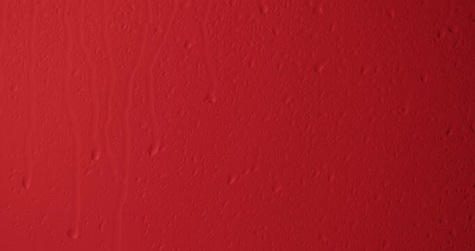 Close up of wet glass with dripping water drops and streaks of rain, on a bright red background, perfect for visual effects and background replacement. Slow motion.