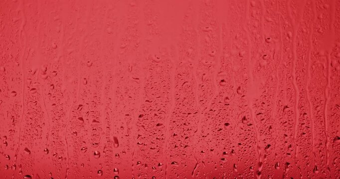Close up of wet glass with dripping water drops and streaks of rain, on a bright red background, perfect for visual effects and background replacement. Slow motion.