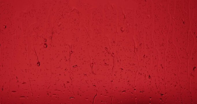 Close up of wet glass with dripping water drops and streaks of rain, on a bright red background, perfect for visual effects and background replacement. Slow motion.