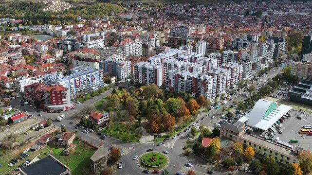 Aerial video of a Kor&ccedil;&euml; roundabout surrounded by colourful trees, roads and nearby buildings in soft seasonal light.