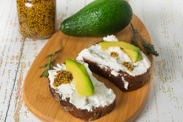 Vegetarian ricotta and avocado sandwiches with grainy mustard on a cutting board. Healthy snack