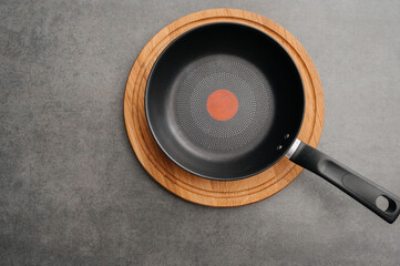Minimalist presentation featuring skillet on textured surface with heat indicator, Stylish arrangement of nonstick pan on cork mat against textured grey background surface