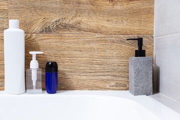 Bottled cosmetics sit on the bathtub. Minimalist modern bathroom interior design.