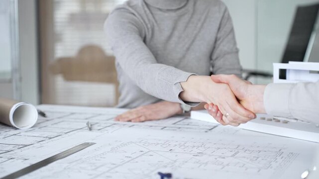 Handshaking between two architects finalizing a construction project deal, business partners agreeing on engineering blueprints and architectural models in an office, close up