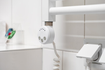 White electric towel warmer with a digital control unit and coiled power cord, providing comfortable heating and energy efficiency for a modern bathroom
