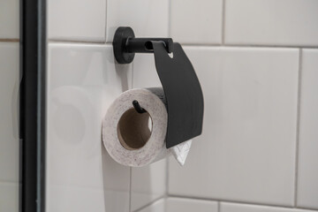 Recycled toilet paper roll on a sleek black metal holder, mounted on a clean white tiled wall, representing bathroom functionality and essential daily hygiene