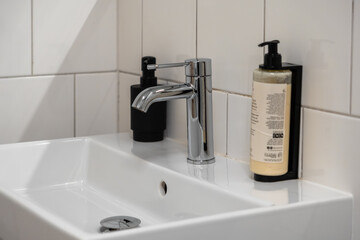 Clean modern bathroom sink with a polished chrome mixer tap and two hygiene product dispensers,...