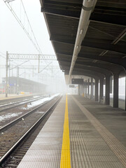 Empty train station platform on a foggy winter morning with tracks extending into the mist, conveying solitude and urban journey