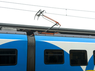 Modern blue and white electric train with an extended pantograph connecting to overhead lines, symbolizing efficient urban public transport and sustainable mobility