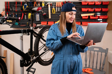 Small business owner using a laptop for bookkeeping in her bike shop. Female entrepreneur managing repair records and inventory on a computer in a garage.