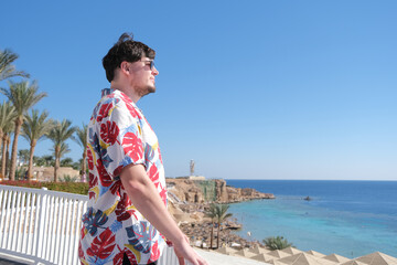 Obraz premium young man in Hawaiian shirt standing on terrace overlooking red sea, Egypt
