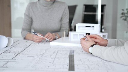 Architectural team analyzing building plans and a white scale model, discussing design concepts and construction details during a professional meeting in an office environment, close up - Powered by Adobe
