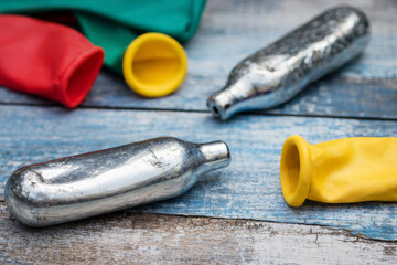 Nitrous oxide cartridges with deflated balloons on wooden table, substance abuse and waste concept