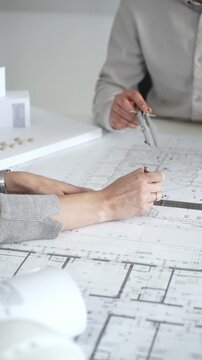 Architects collaborating on engineering blueprints and architectural drawings for a modern building project, planning urban construction development with a scale model, close up