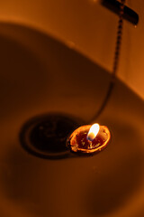 A burning candle in a shell floats on the water surface in a sink.
