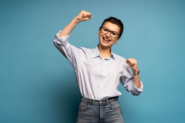 Extremely happy woman standing with raised clenched fists, winning lottery, celebrating her success isolated on blue