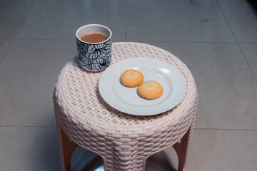 A cup of coffee with milk and two biscuits on a plastic stool at home