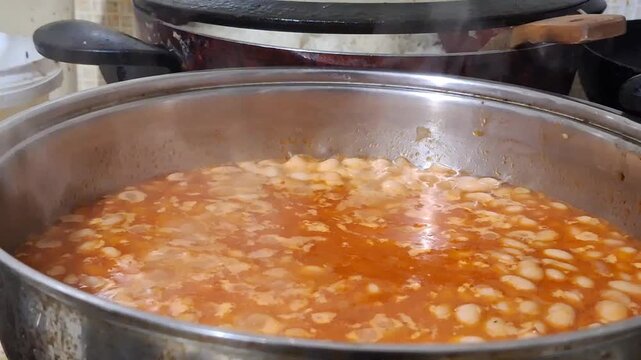 Close up of traditional Turkish white bean stew (Kuru Fasulye) simmering in a metal pot on a kitchen stove