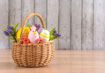 Happy easter holidays greeting card template; wicker basket with easter eggs and flowers on a wooden table against wooden background; copy space