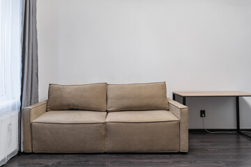 stylish studio apartment with minimalist design. gray curtains on large window, a beige sofa near the wall, and a bedside table. The apartment has white walls and a dark floor.