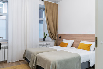 The interior of the studio apartment has two beds with wooden headboards, lamps, white linens and yellow pillows. The design of the hotel room.