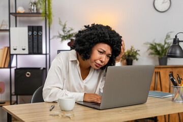 African American businesswoman at home office frowns at laptop upset by game defeat fail, rejection email. Freelancer girl at table sighs plans recovery seeking motivation and new goals after setback