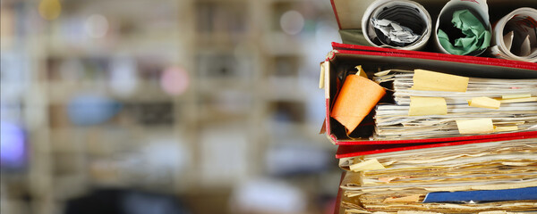 Stack of grungy messy file folders, blurred office in the back,red tape, bureaucracy,aministration,business concept