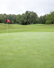 Obraz premium Freshly cut green golf course with red flag on the putting green under cloudy sky in late afternoon