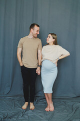 Fototapeta premium Couple stands together holding hands while expecting a baby in a studio with blue background during daytime