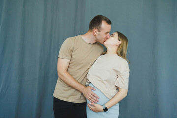 Fototapeta premium Couple shares a moment of love and connection as they prepare for parenthood in a simple indoor setting with a blue backdrop