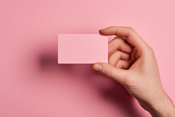 A hand holds a blank pink rectangular card against a matching pink background