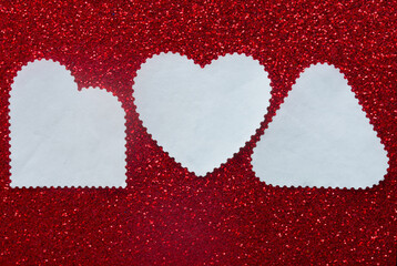 Top view of clean white paper shapes including a heart on sparkling red texture. Creative mockup for love letter, wedding invitation or romantic note with copy space. Photo
