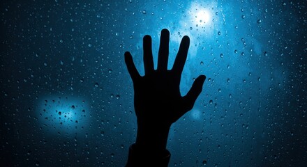 Silhouette of a hand touching a rain-streaked windowpane against a bright blue light