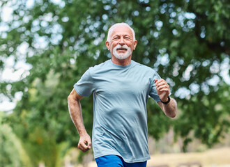 Smiling active mature elderly man jogging running in the park