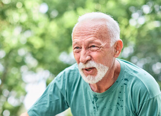 Portrait of a mature senior man exercising in a park, tired mature male running and taking a break outdoors, healthy lifestyle and cardio exercise in nature concepts, vitality and active senior