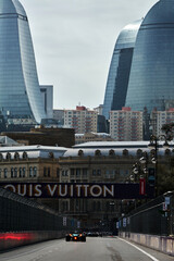 Naklejka premium BAKU, AZERBAIJAN - SEPTEMBER 19, 2025: A Formula 1 car competes during the Azerbaijan Grand Prix at the Baku City Circuit. The iconic Flame Towers and a large Louis Vuitton sponsorship banner