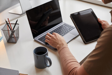 Close-up of man sitting at the table typing on laptop and connecting tablet pc with computer