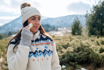 Beautiful woman applying sunscreen stick  in the winter mountain