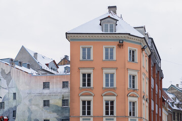 Fototapeta premium Historic Old Town Riga apartment building with orange facade white window frames and snow topped roof representing preserved urban architecture and winter city environment