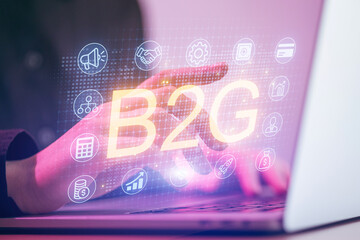 Hand interacts with digital display featuring B2G concepts and icons on a laptop screen in a modern workspace