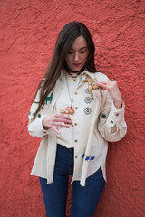 Woman wearing a traditional Ukrainian vyshyvanka holding handmade straw didukh toys against a textured red wall, symbolizing Ukrainian folk traditions, seasonal rituals, and cultural heritage.