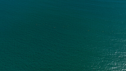 A minimalist aerial view of the deep emerald sea. Gentle ripples create a surface with subtle light...